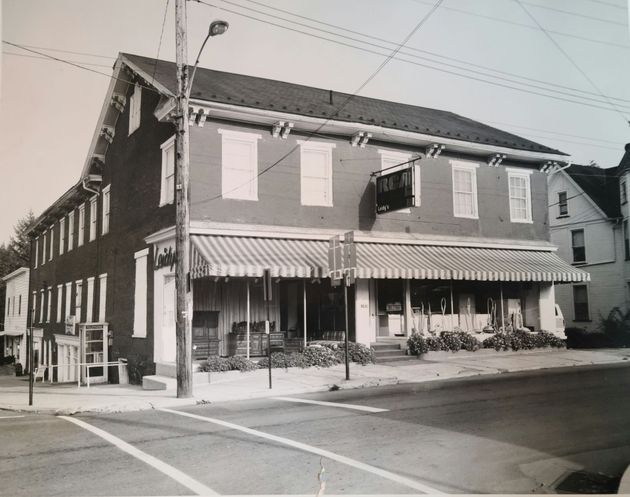 Black-and-white street view of a two-story brick building with striped awnings on a corner lot.