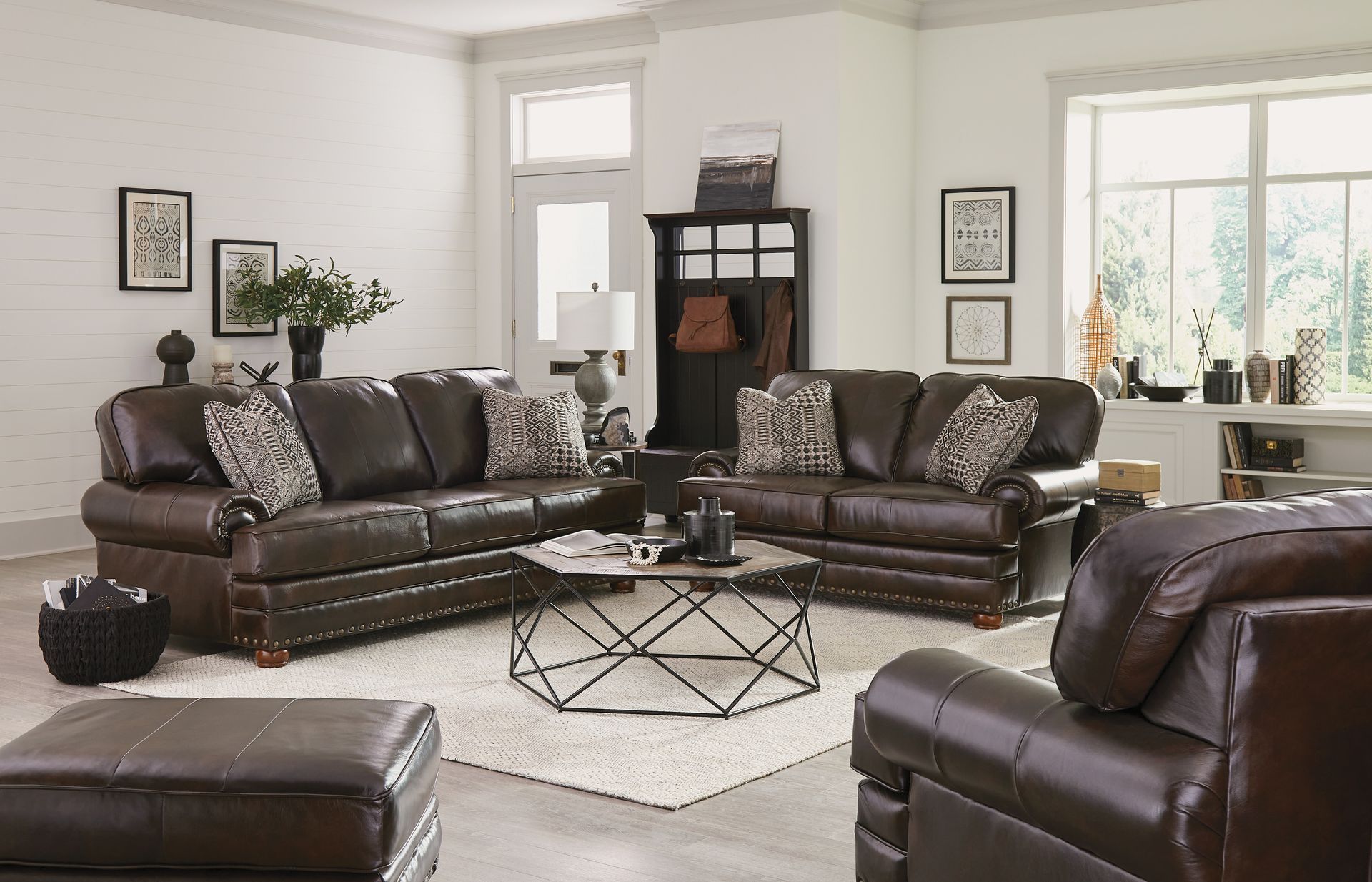 Brown leather living room set in a bright, neutral room with a coffee table and large windows
