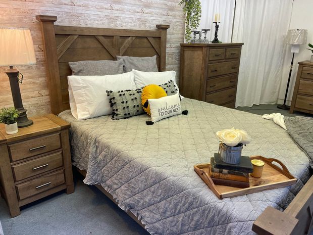 Cozy bedroom with a gray quilted bed, wooden nightstands, dresser, and brick accent wall