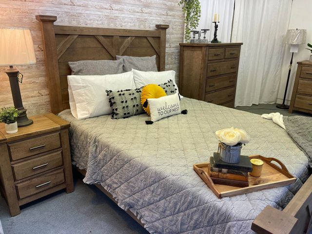 Cozy bedroom with a gray quilted bed, wooden nightstands, dresser, and brick accent wall