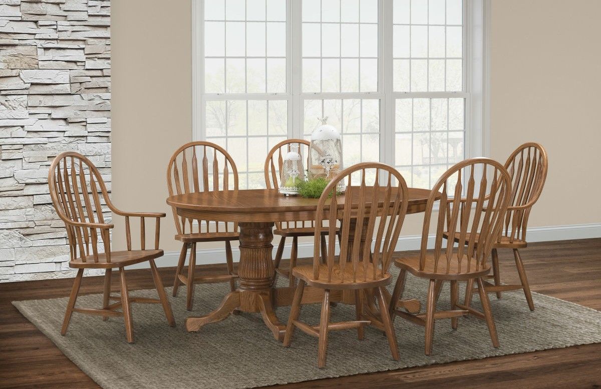 Wooden dining table with six chairs in a bright room by large windows and stone accent wall