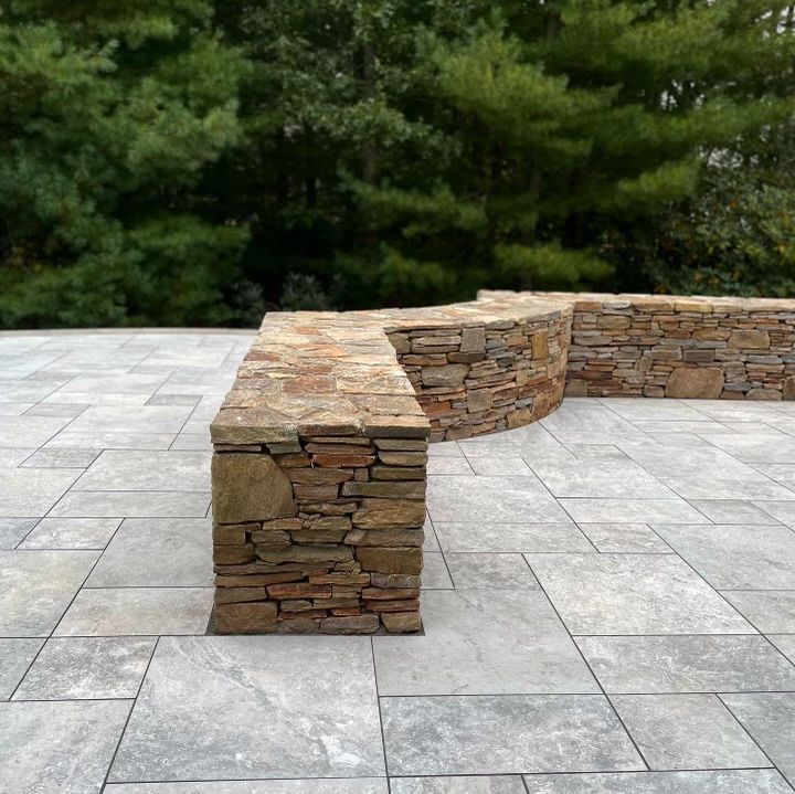 A stone bench is sitting on a tiled patio next to a stone wall.