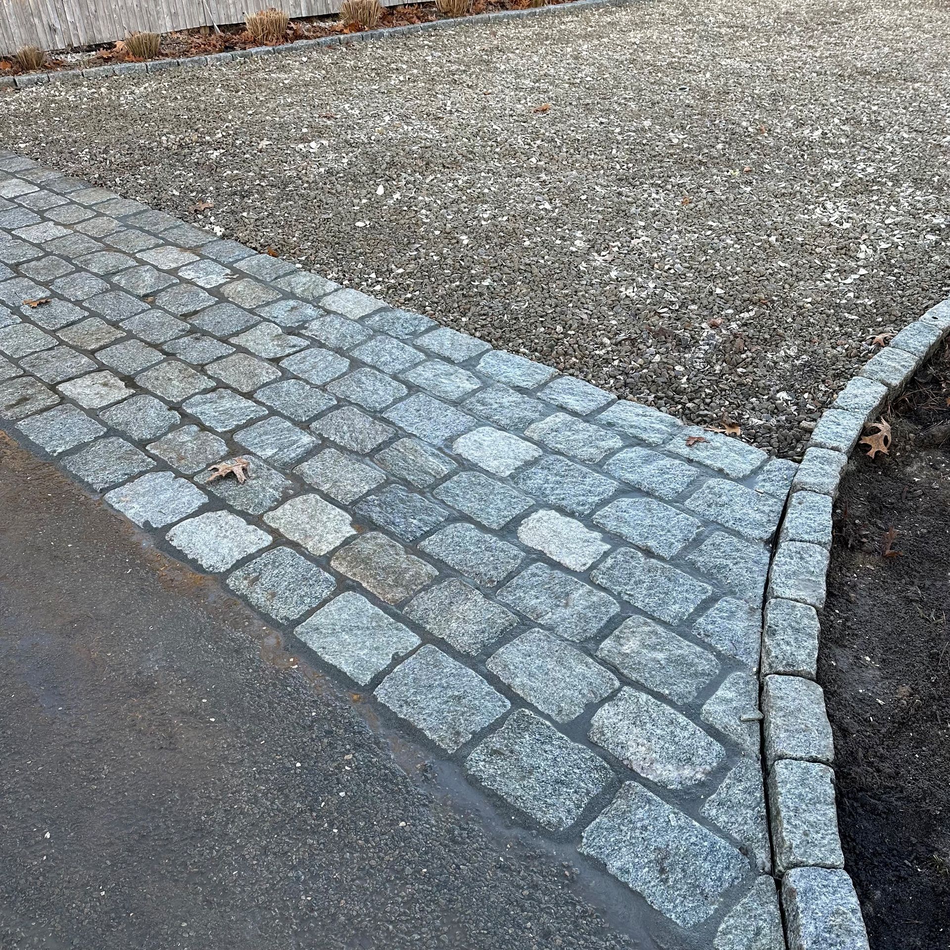 A cobblestone walkway leading to a gravel driveway.