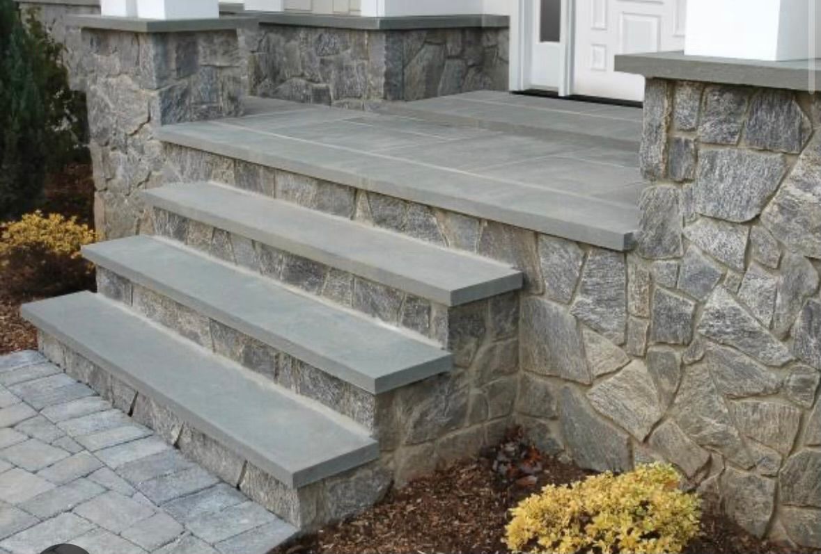 A stone porch with stairs leading up to it and a stone wall.