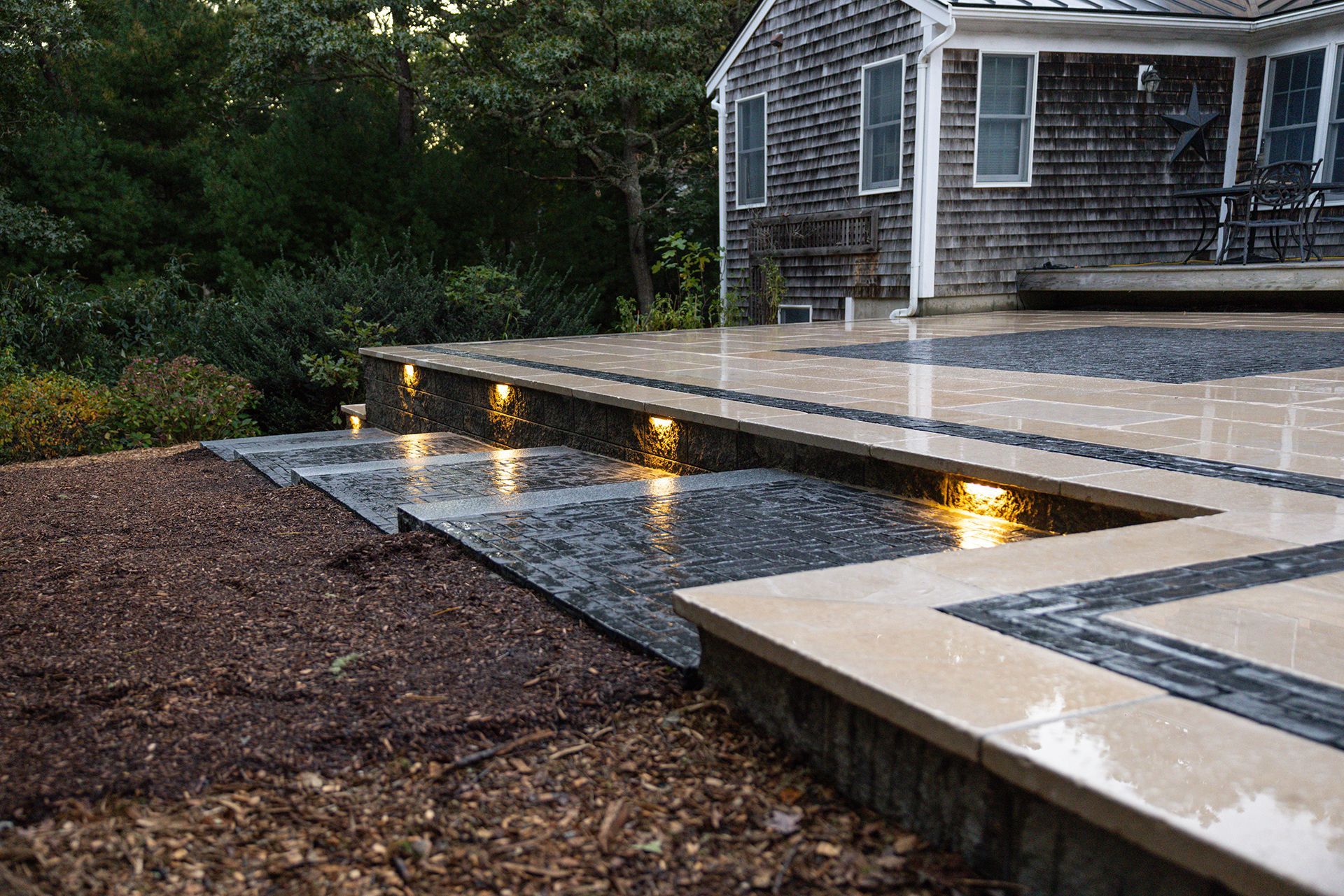 Outdoor patio with tiered steps, built-in lights, and mulched landscaping in front of a house.