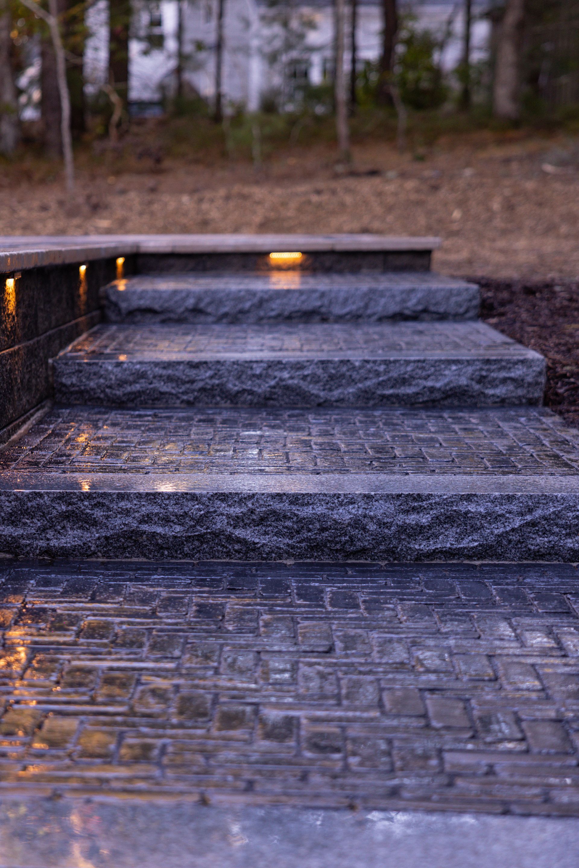 Dark stone steps with built-in lights leading up from a paved patio, outdoor setting.