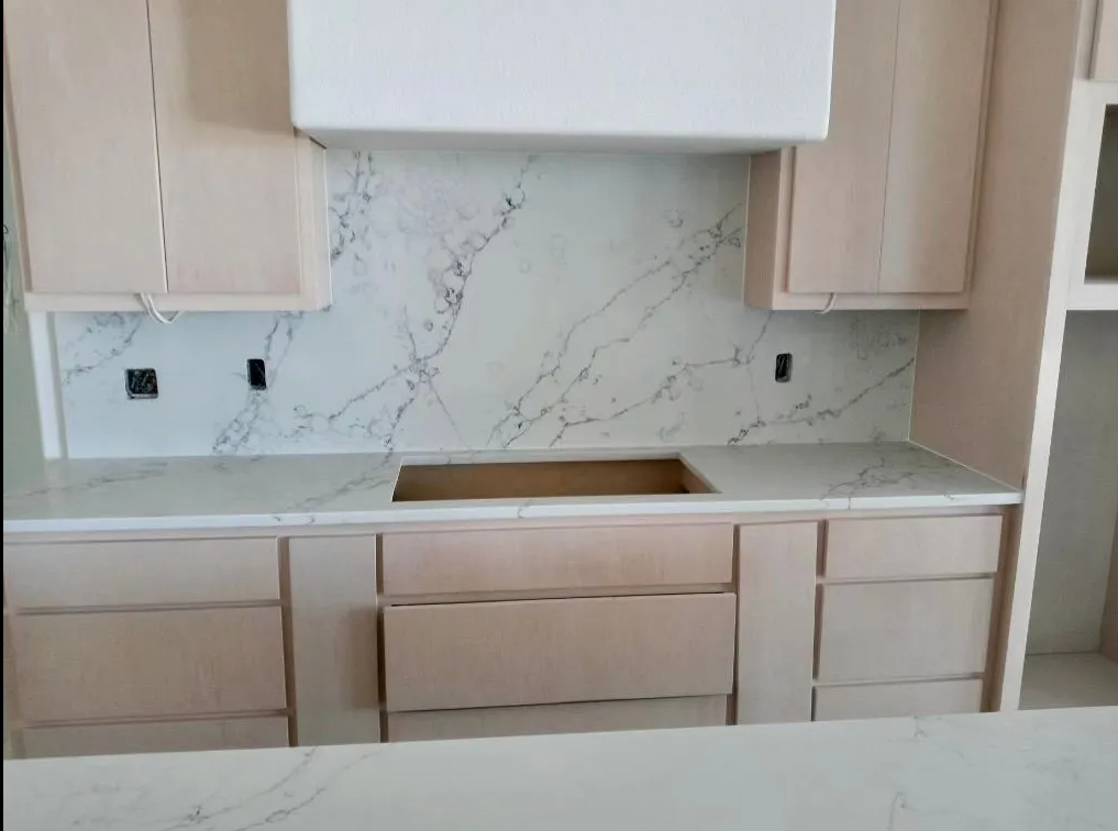 Modern kitchen with white cabinets, marble backsplash, and unfinished countertop with sink cutout