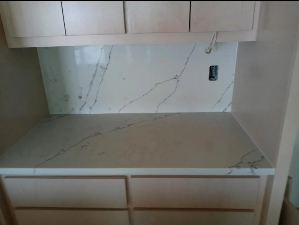 Empty kitchen countertop with white marble backsplash and light wood cabinets
