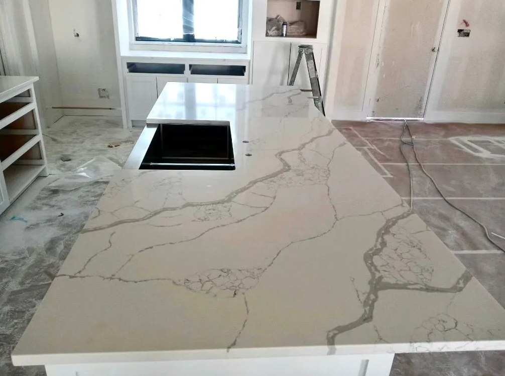 Marble kitchen island with waterfall countertop and black cooktop in a bright room under renovation