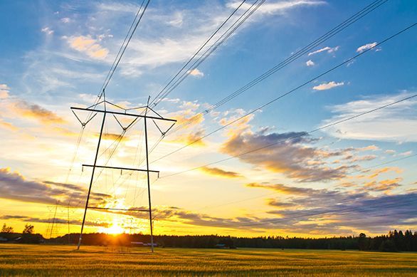 A sunset over a field with power lines in the foreground.