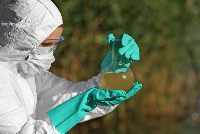 A person in a protective suit is holding a beaker of liquid.