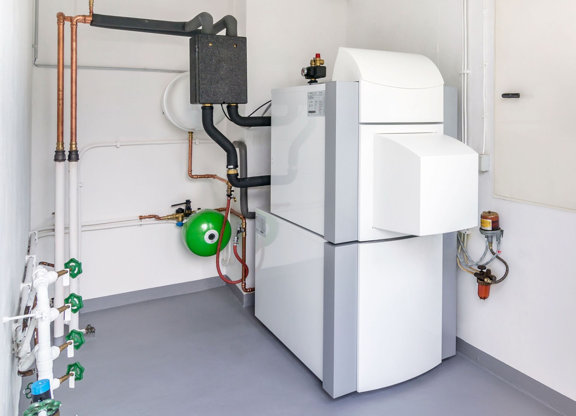 White and grey industrial heating system in a utility room with copper and black piping.