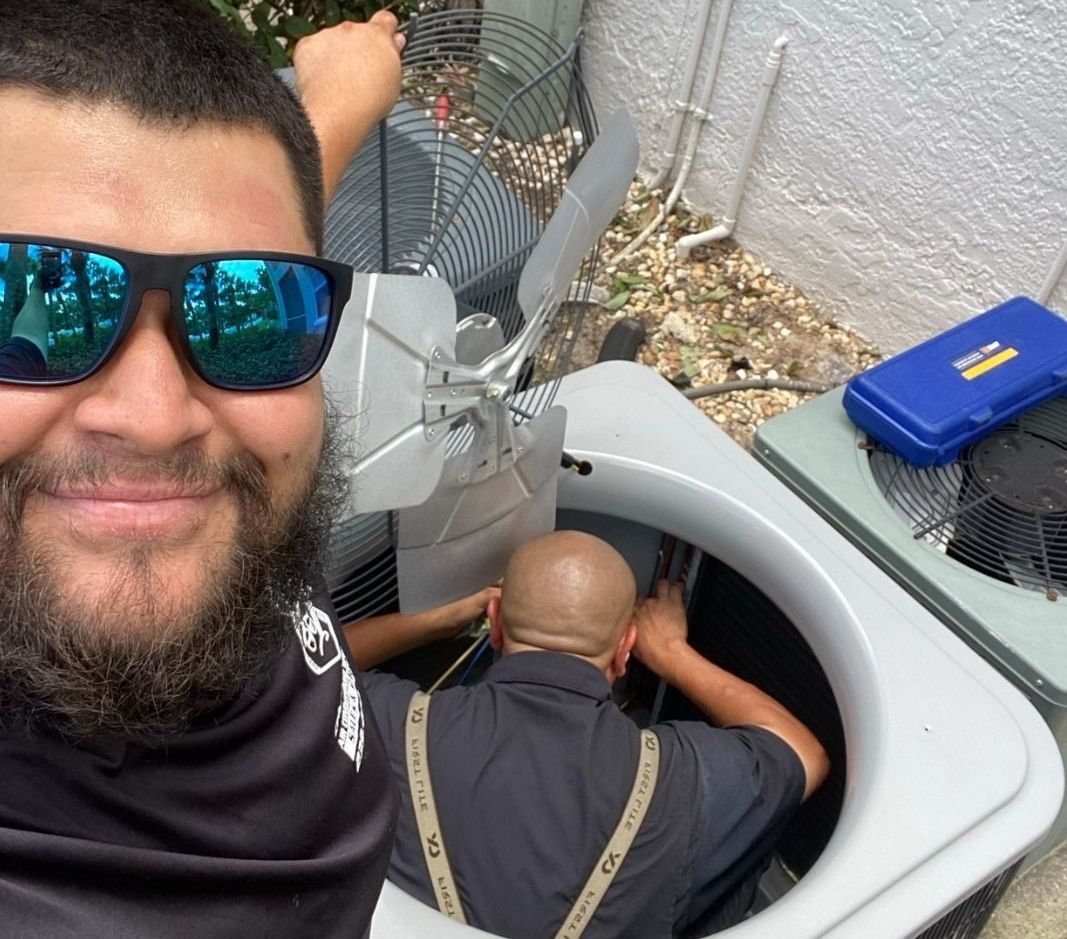 A man wearing sunglasses is taking a selfie with another man in an air conditioner.