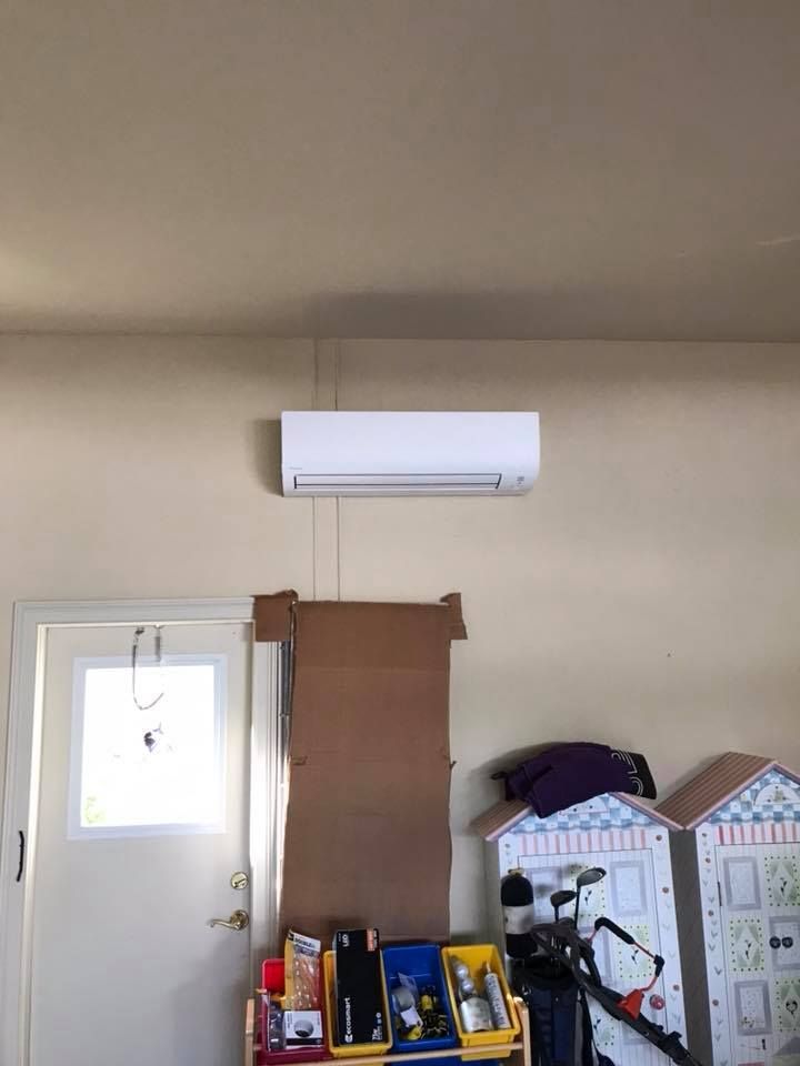 A white air conditioner is hanging from the ceiling of a garage.