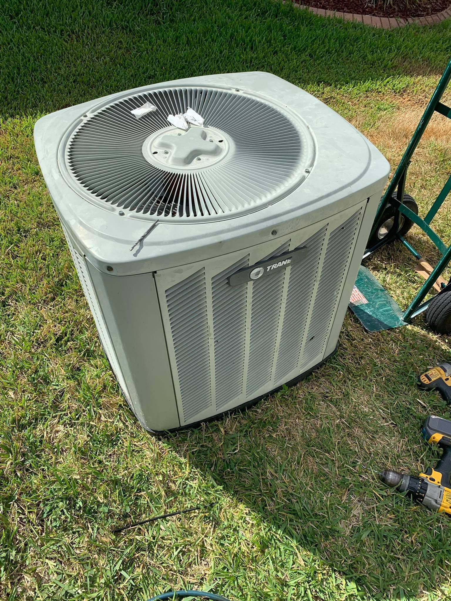 A white air conditioner is sitting on top of a lush green lawn.