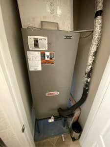 A gray air conditioner is sitting in a closet next to a door.