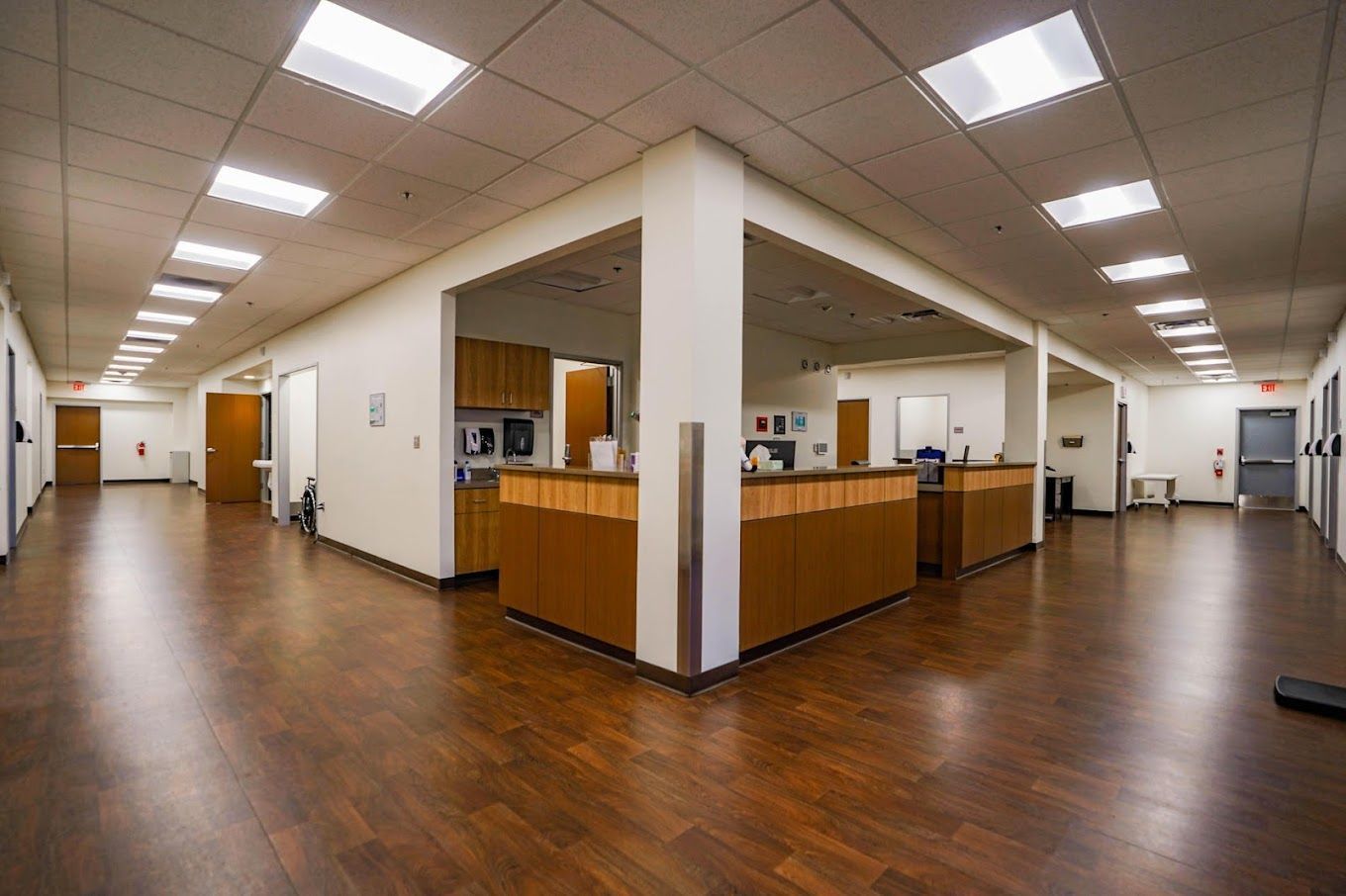 A long hallway in a hospital with wooden floors and white walls.