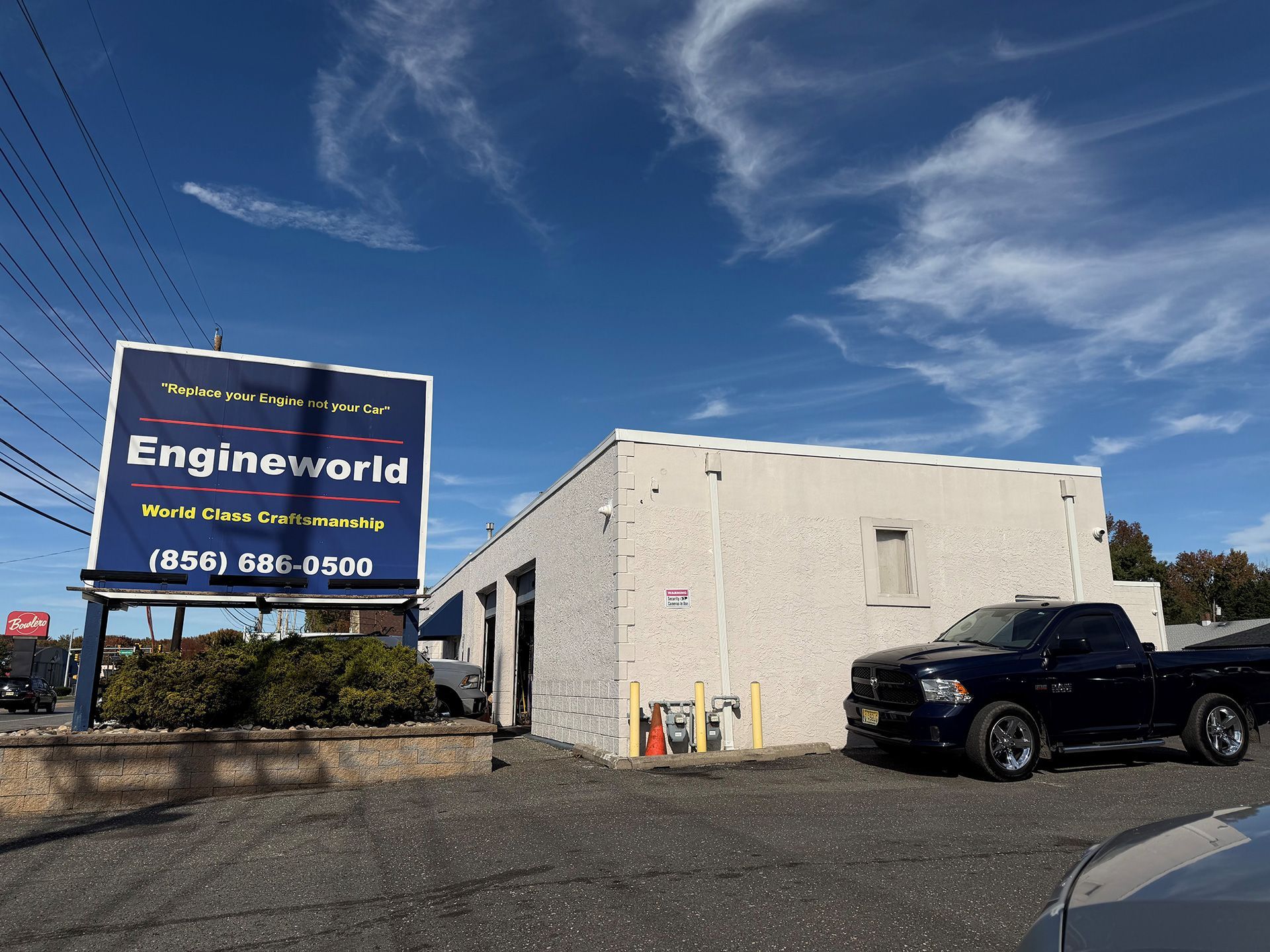 Enginesworld sign beside a white building and black pickup truck under a blue sky
