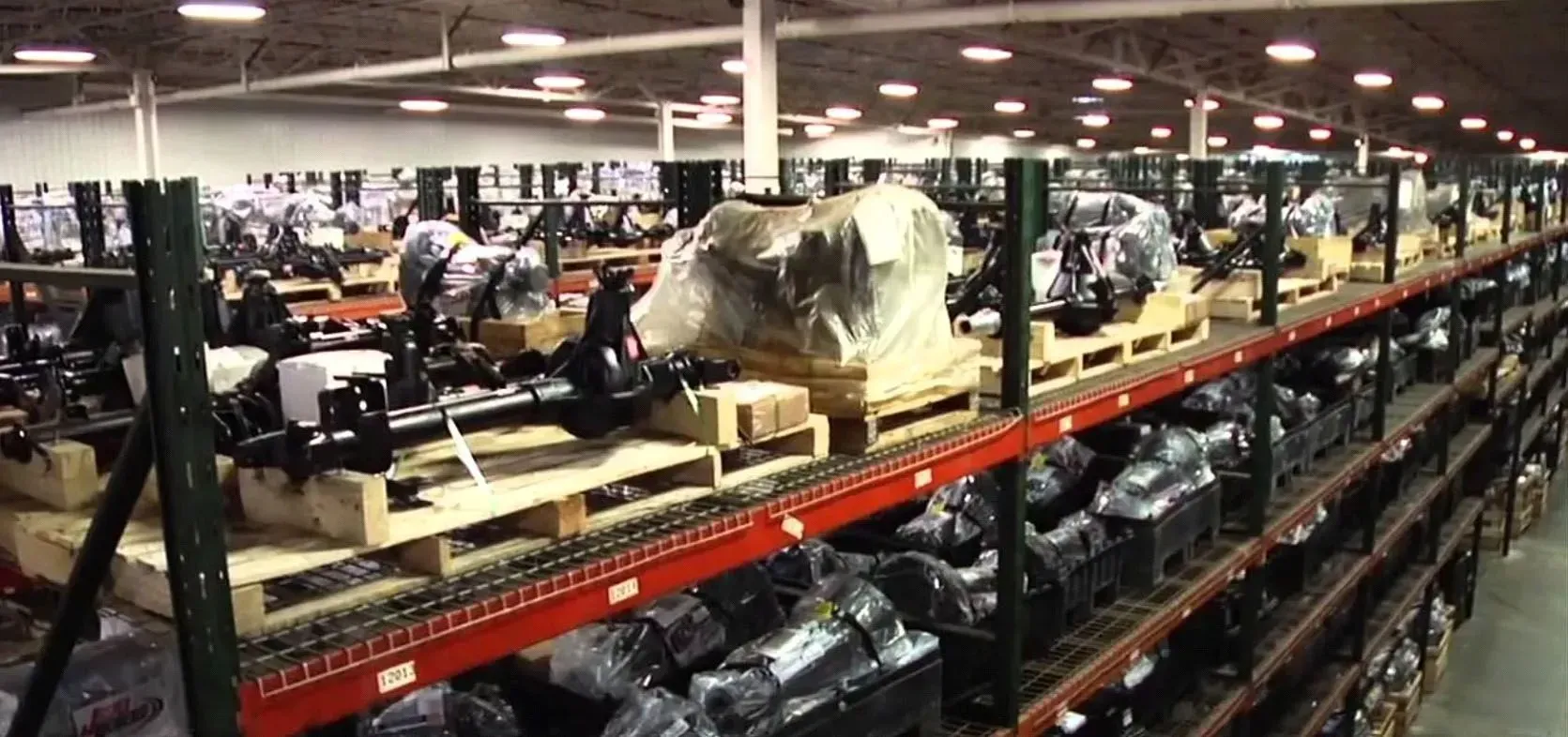 Warehouse with stacked auto parts on shelves; workers load and organize parts.