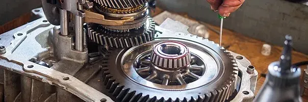 Gears and parts of a transmission being repaired. A hand holds a tool.