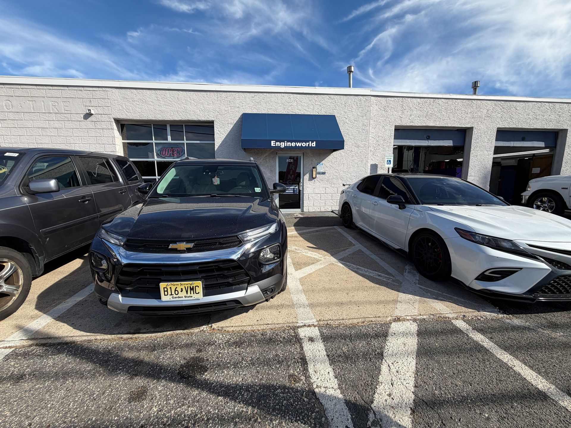 Cars parked outside a blue-roofed auto repair shop on a sunny day.