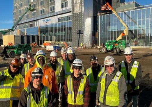 Construction crew in high-visibility vests and hard hats gathered at an urban worksite.