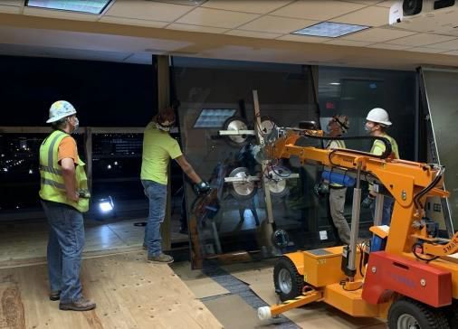 Workers in safety vests and hard hats inspect machinery inside a dim industrial room with an orange lift.