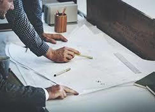 Two people reviewing architectural plans on a desk with pencils and paper tools