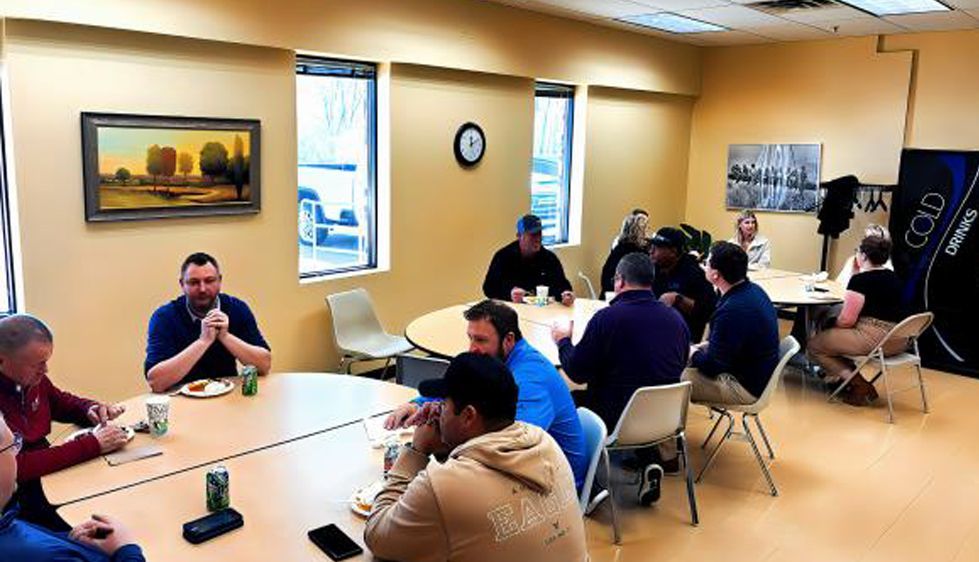 People seated around tables in a meeting room, discussing in a casual group setting.
