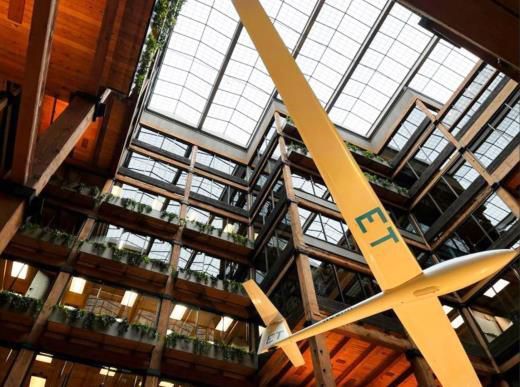 Yellow airplane suspended in a glass-roofed atrium with industrial walls and walkways