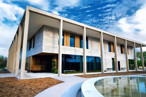 Modern white building with large windows beside a curved reflecting pool under a blue sky