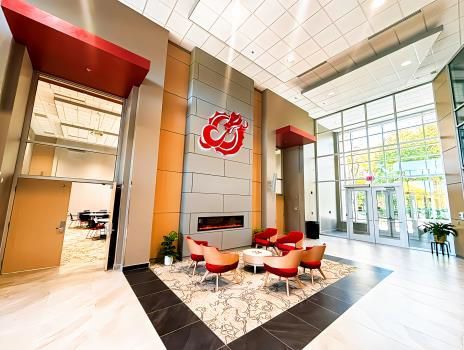 Modern lobby with red chairs, marble floor, tall windows, and a red wall logo by the entrance