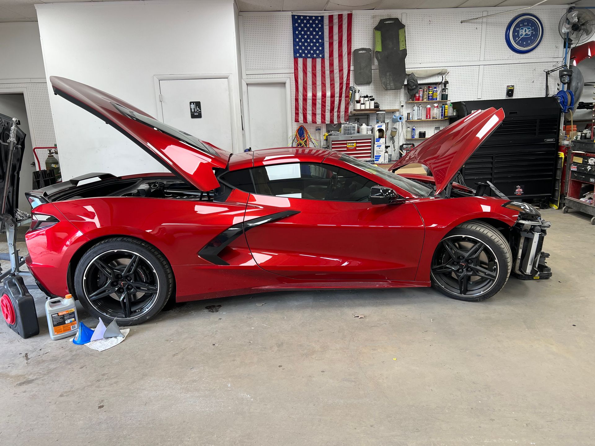 A red sports car with the hood up is parked in a garage.