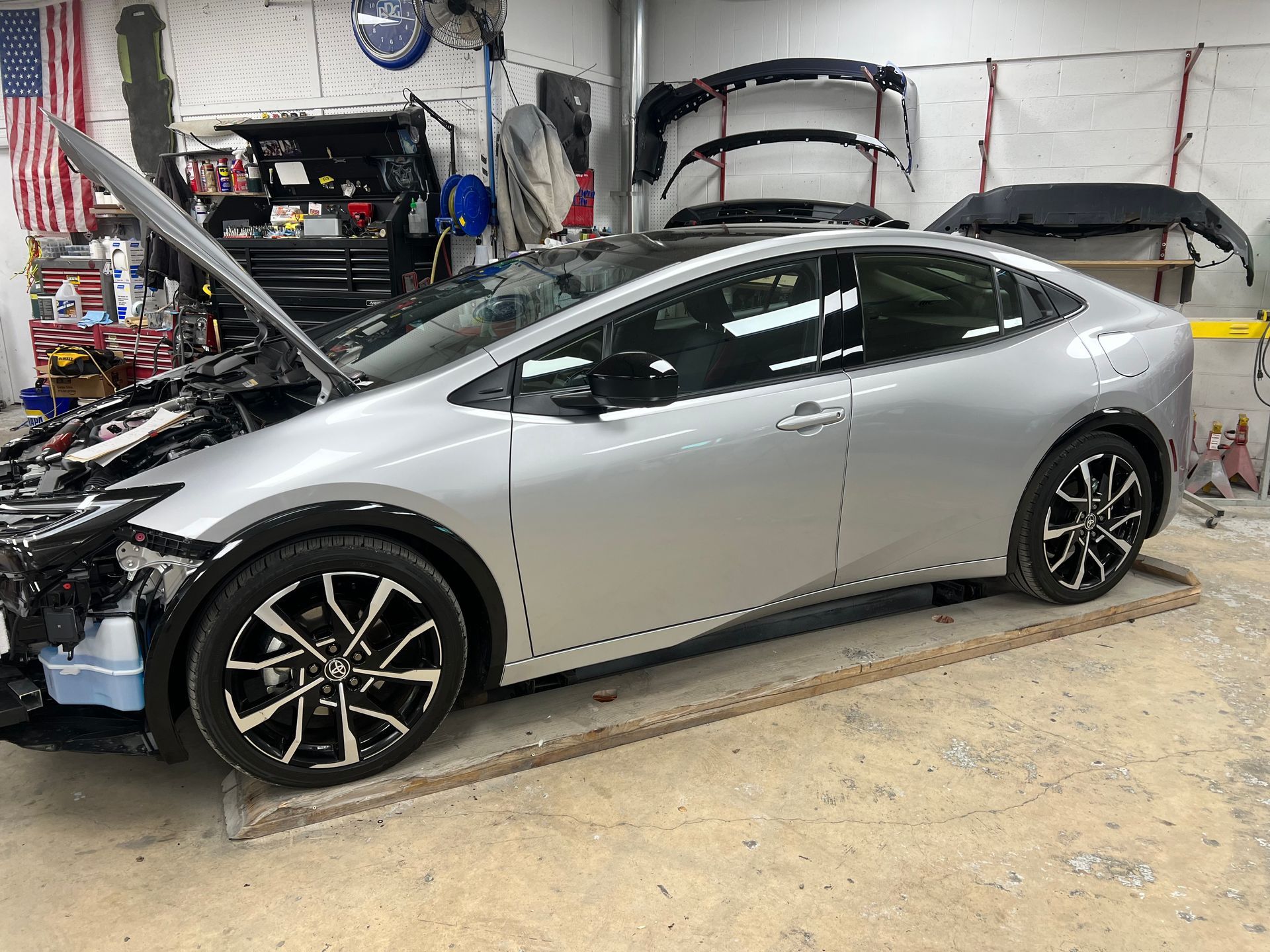 A silver car is sitting in a garage with its hood open.
