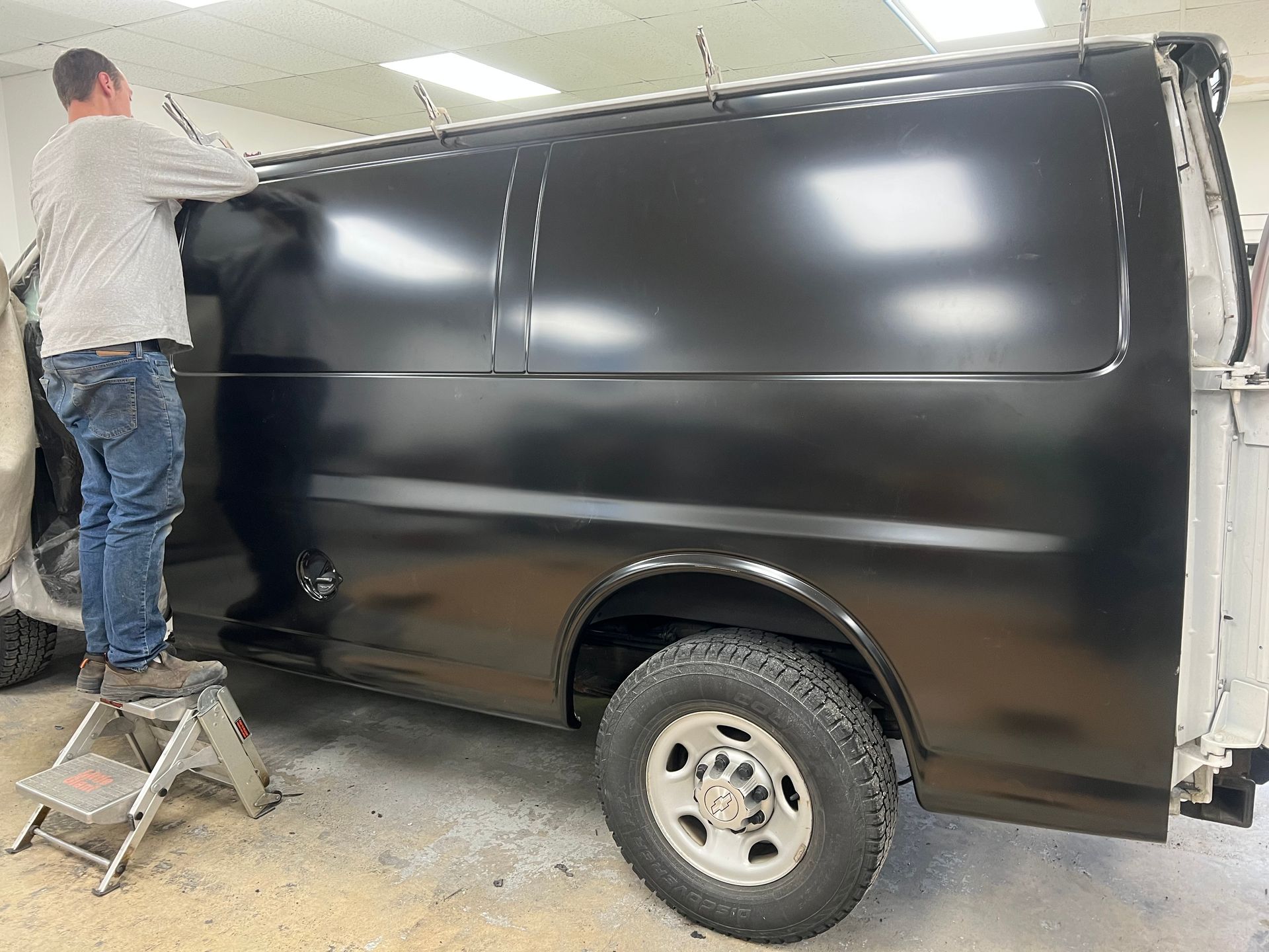 A man is painting a black van in a garage.