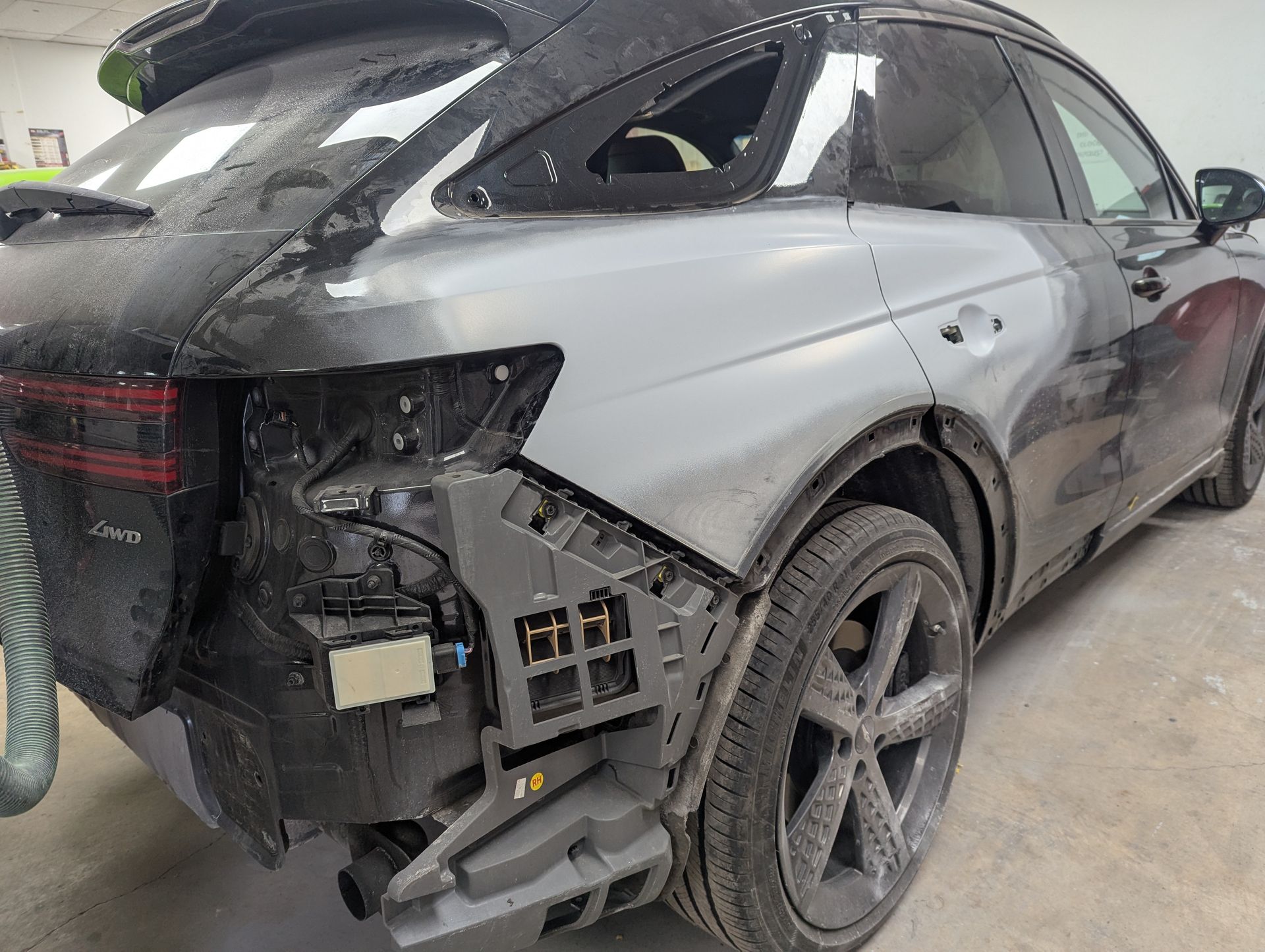 A black car with a damaged rear end is sitting in a garage.