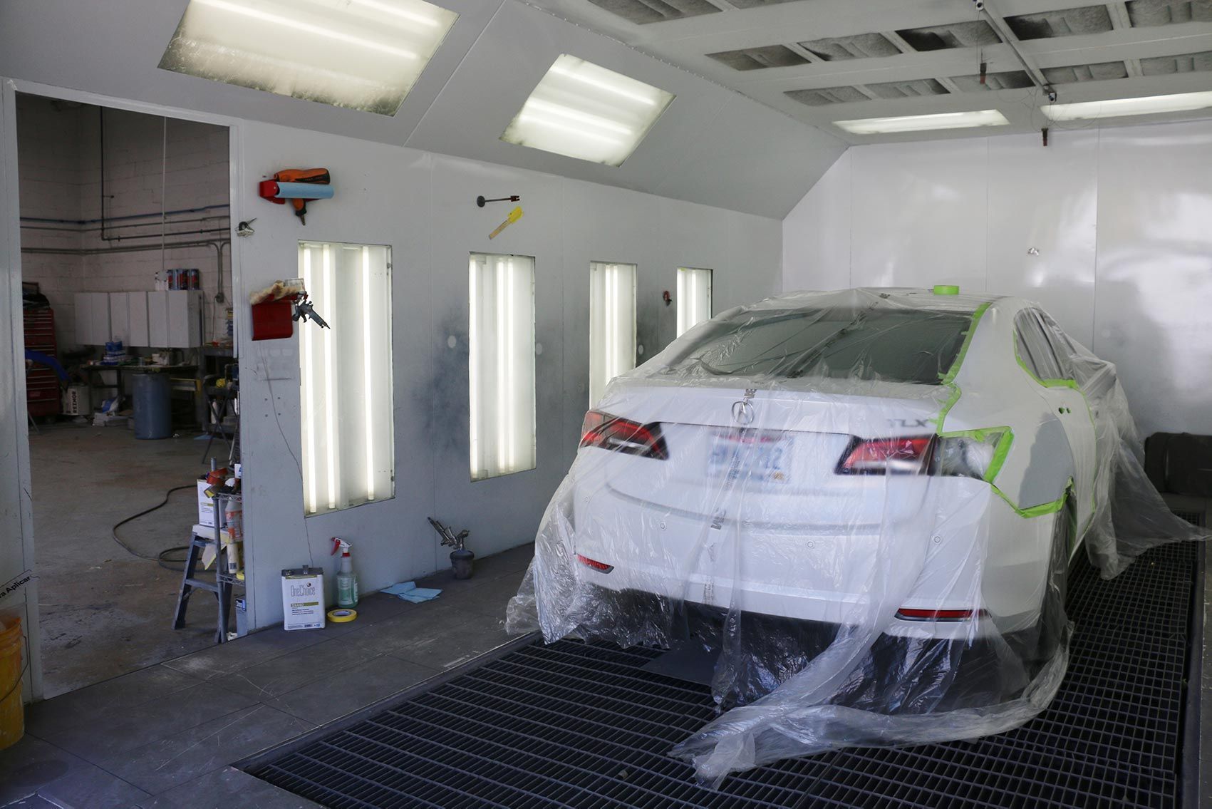 A white car is wrapped in plastic in a paint booth.