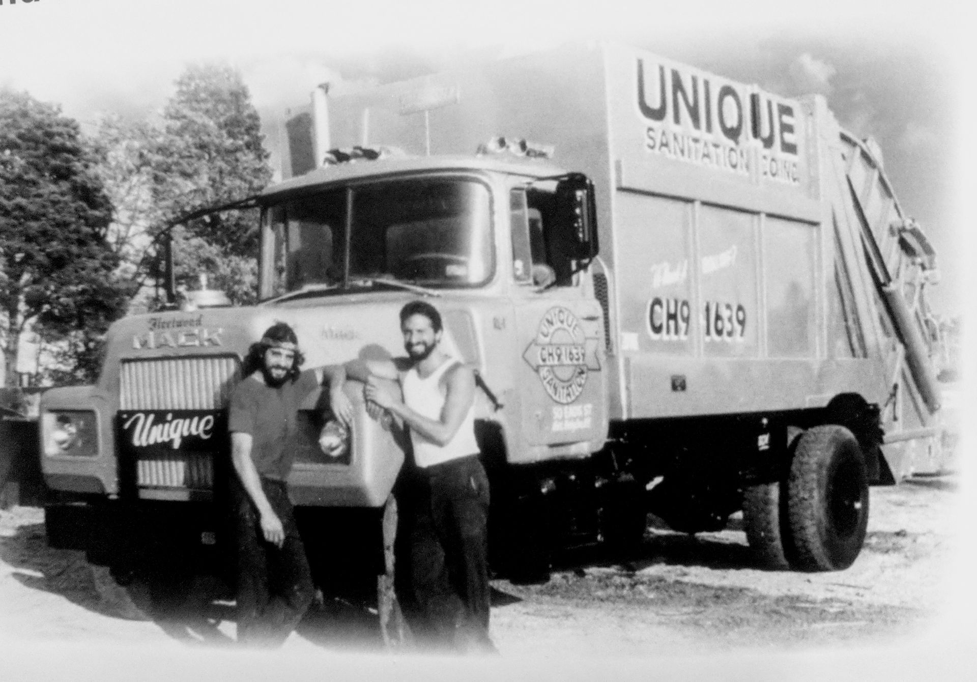 Two men standing in front of a unique garbage truck