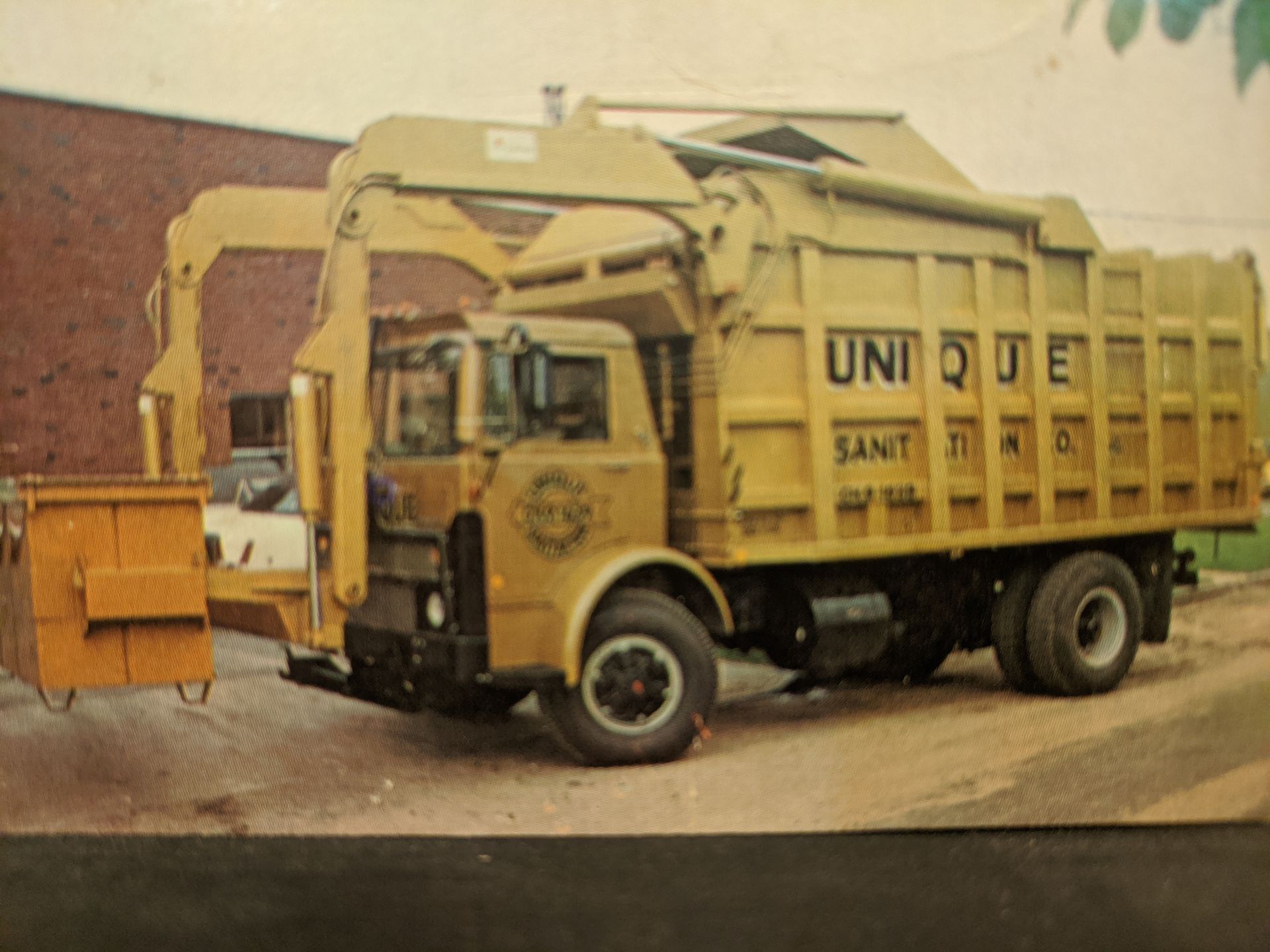 A yellow garbage truck with the word unique on the side is parked in front of a building.