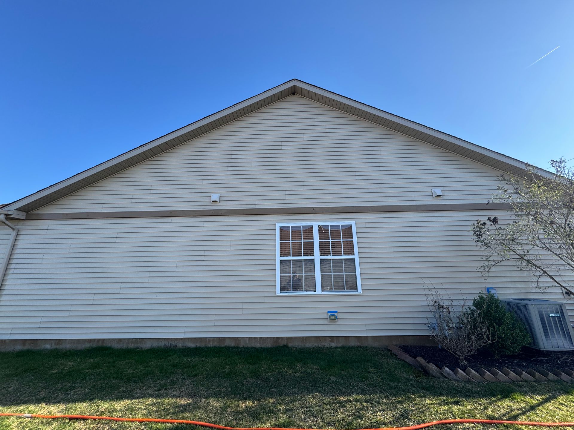 Tan house siding with a window, grass, and an AC unit.