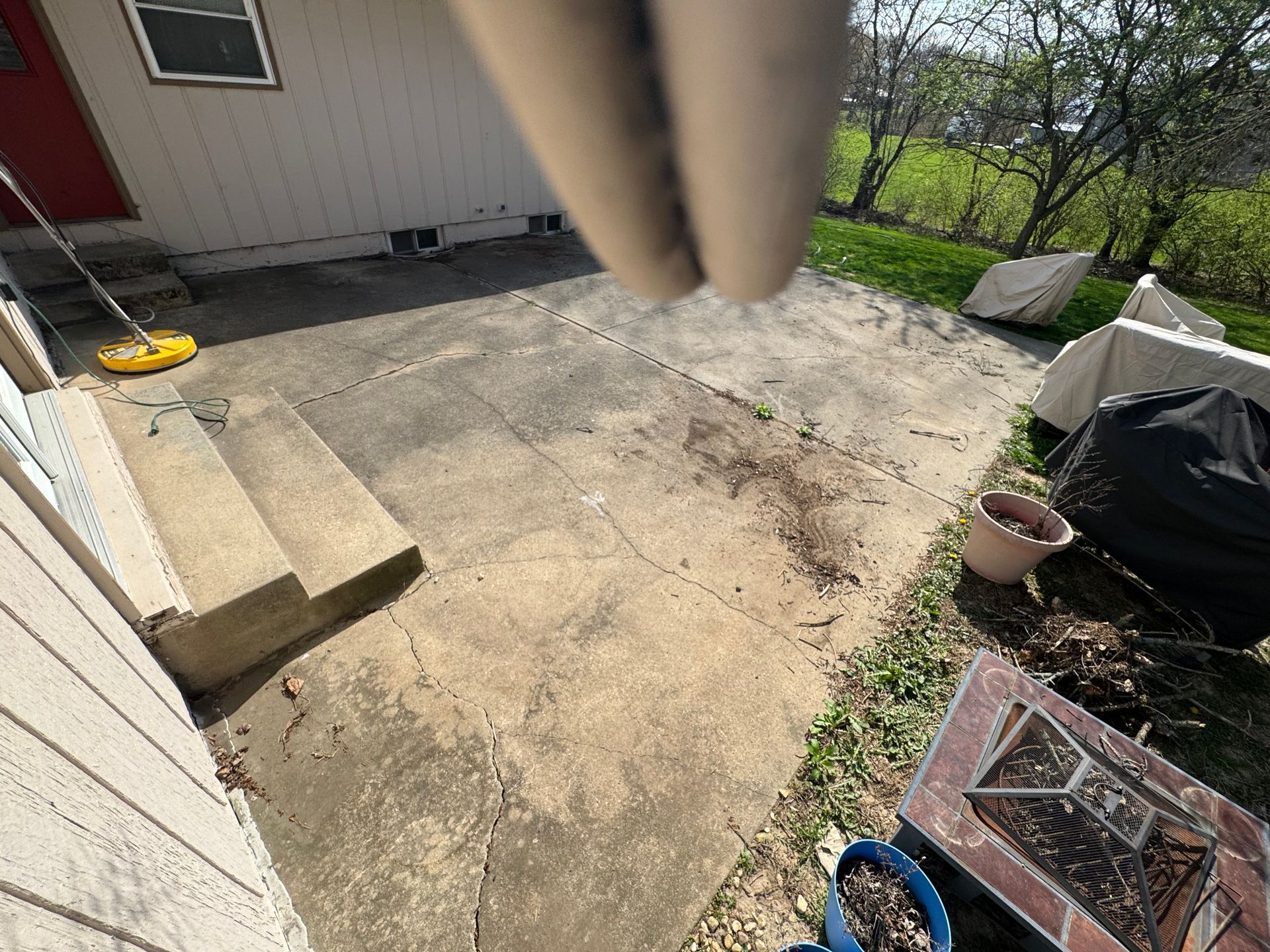 Concrete patio next to a building with steps, covered items, and debris.
