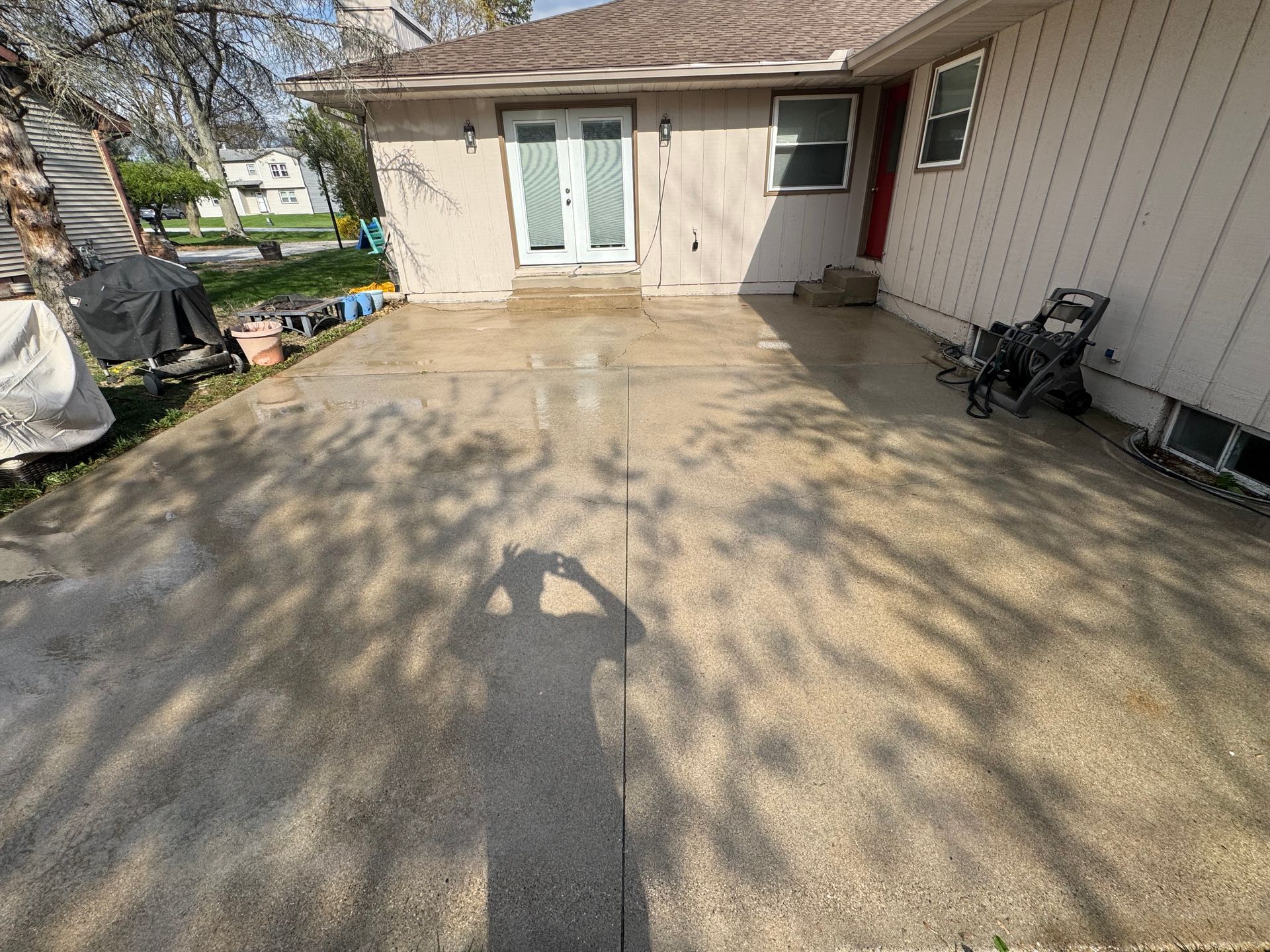 A concrete patio with a shadow of a person, next to a house with double doors and a window.