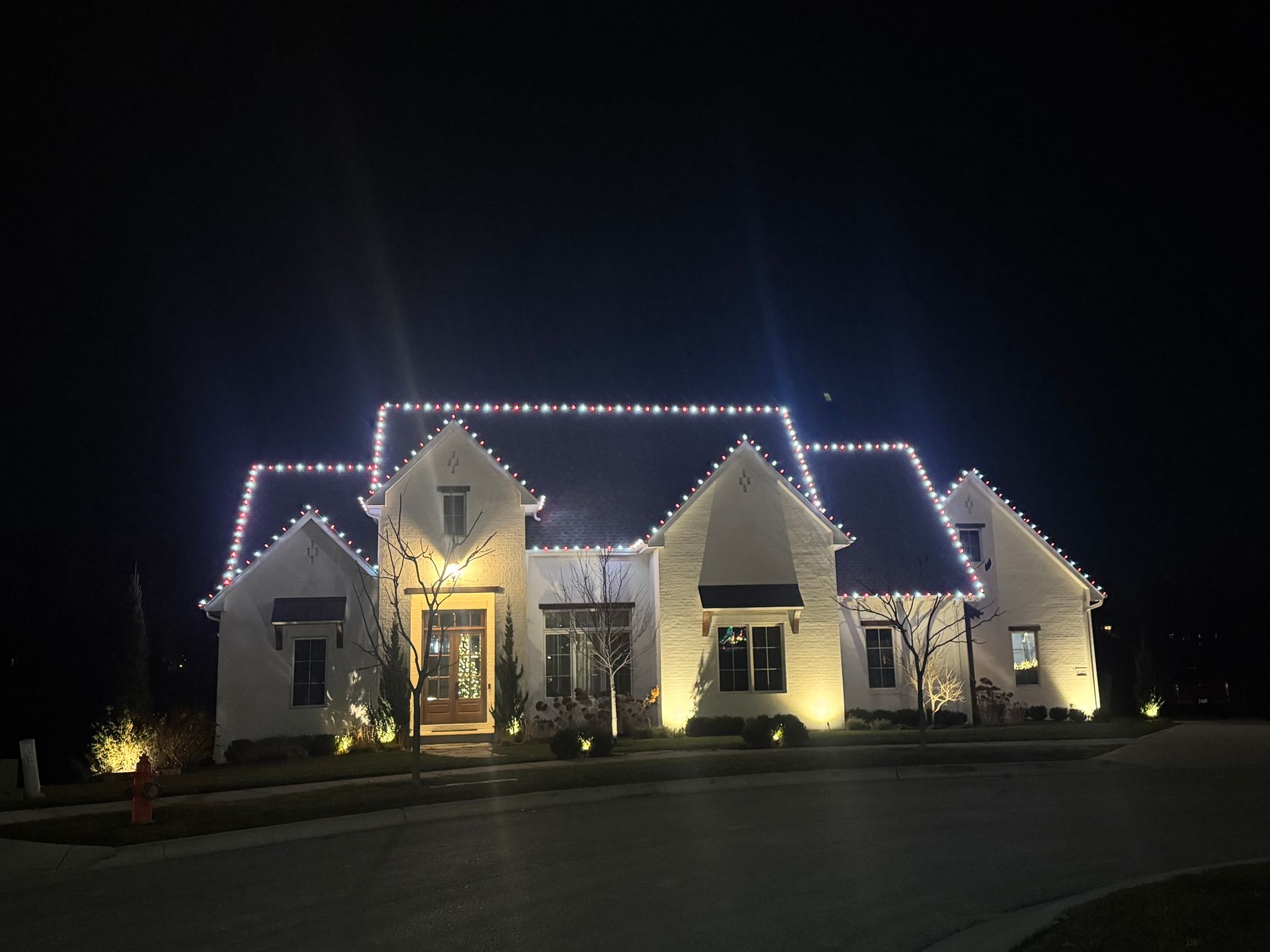 White house at night, illuminated with white Christmas lights along the roofline and spotlights.