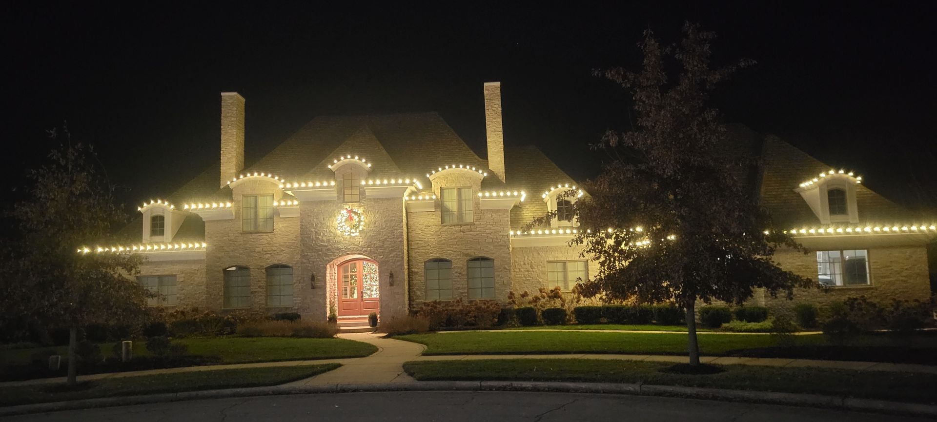 A large house at night decorated with white Christmas lights on the roofline.