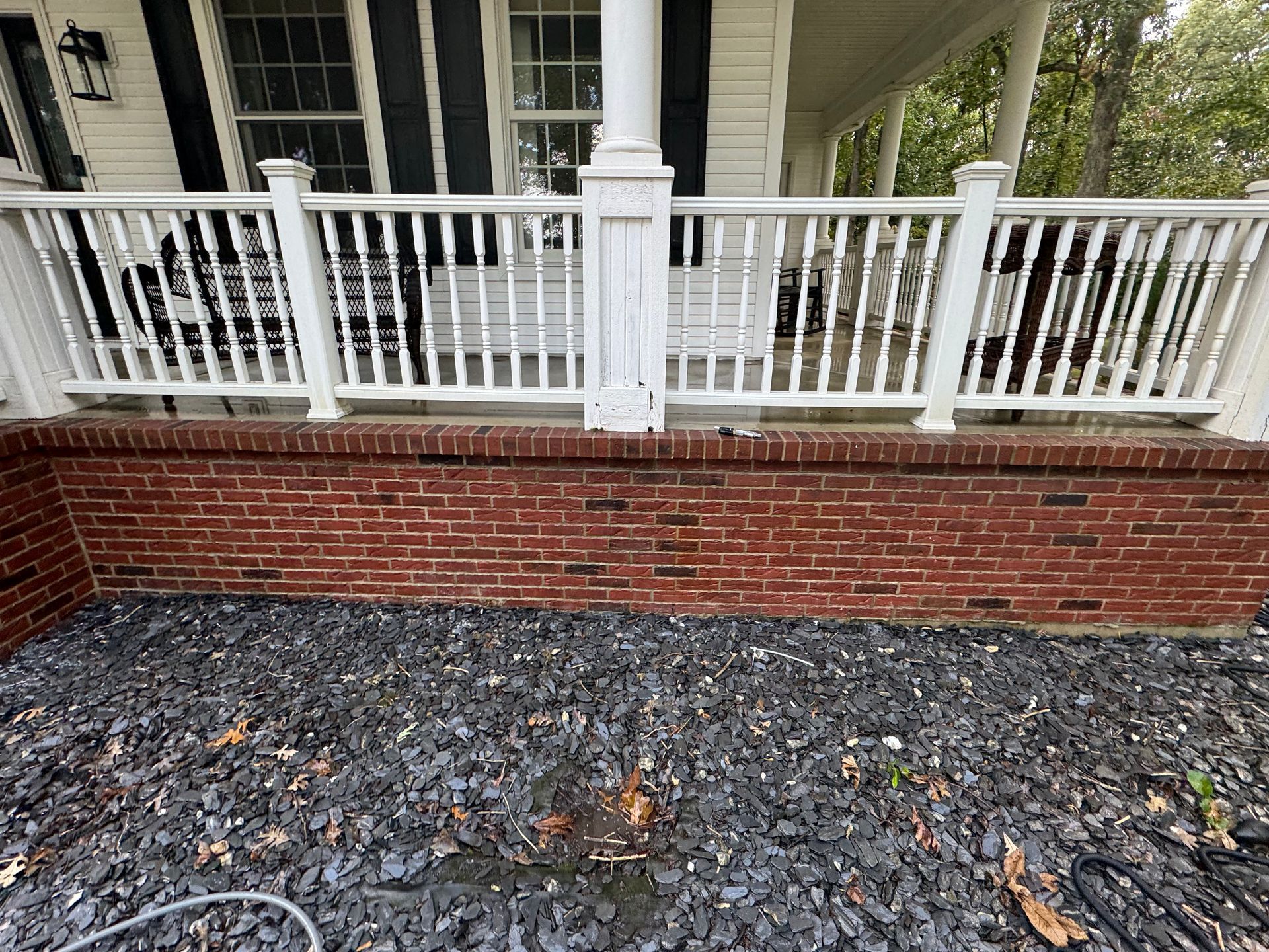 White porch with a red brick base and black gravel.