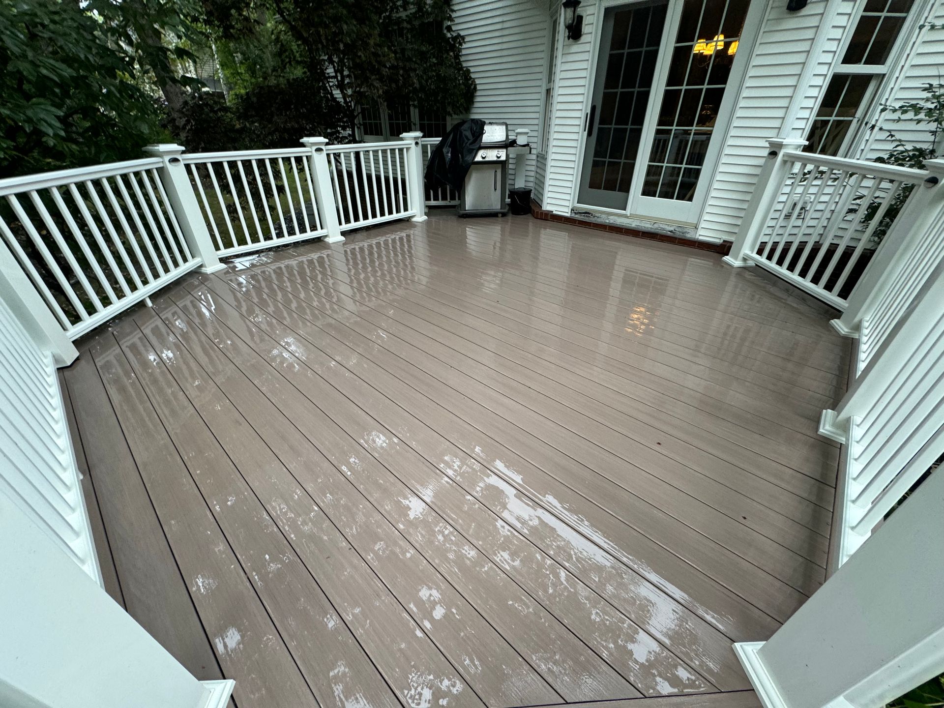 Wet wooden deck with white railing, next to a white house with glass doors.