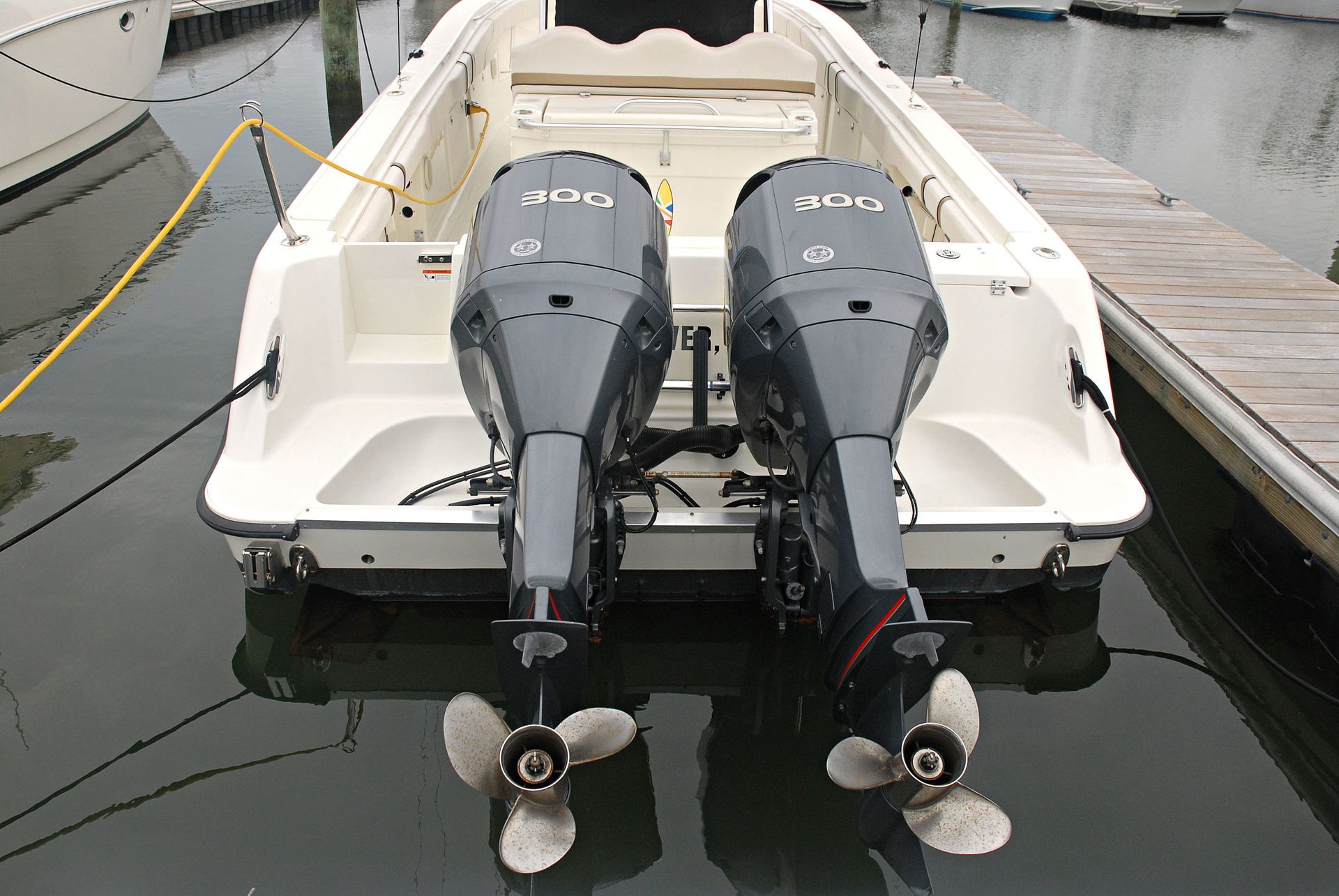 Rear view of a white powerboat docked at a marina with twin outboard motors labeled “300.”