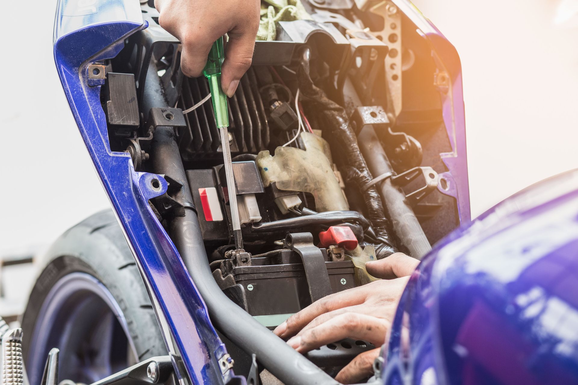 Person using a screwdriver to secure a motorcycle battery inside the vehicle’s engine compartment.