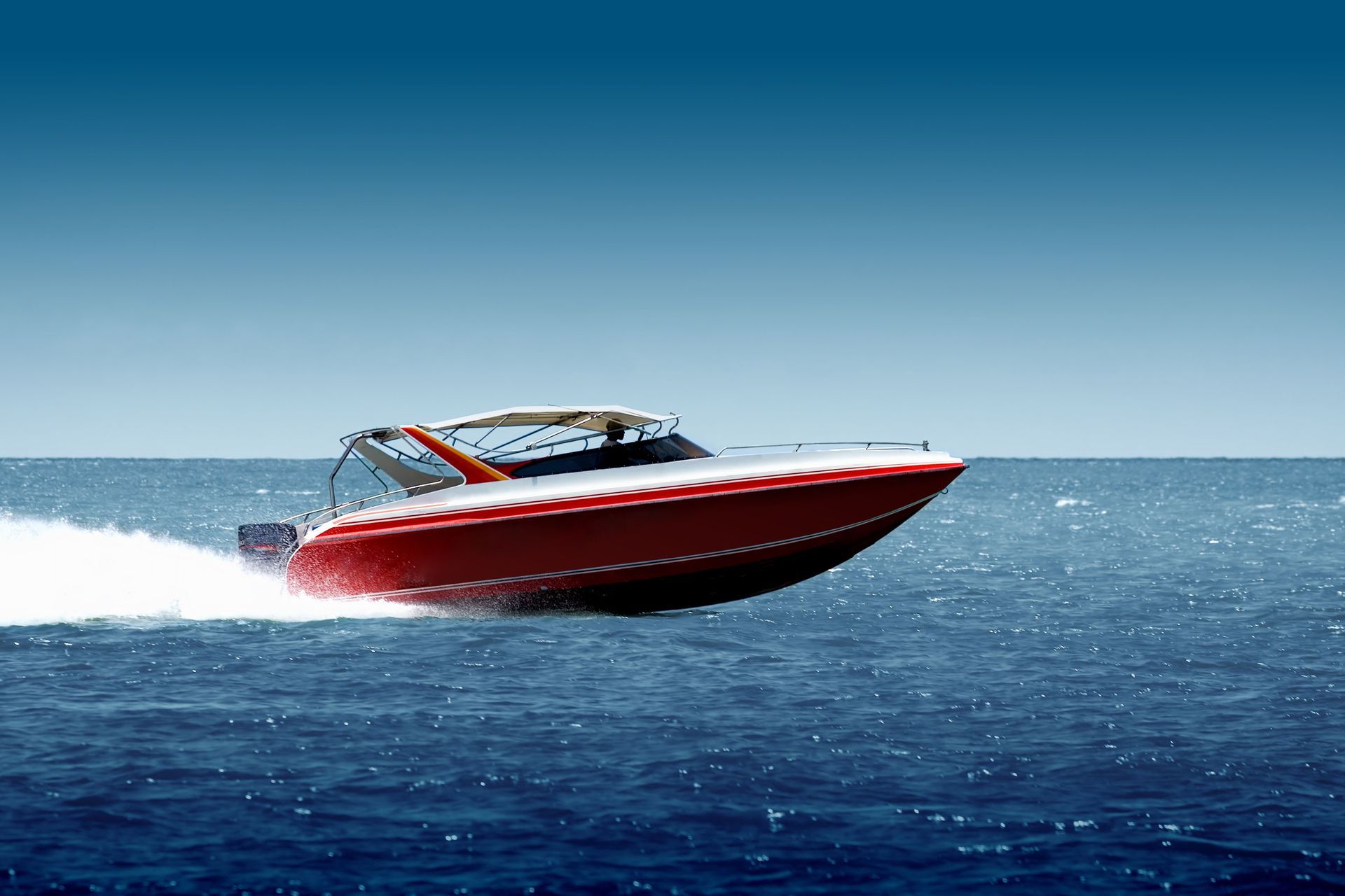 Red speedboat gliding quickly across blue ocean water under a clear sky.
