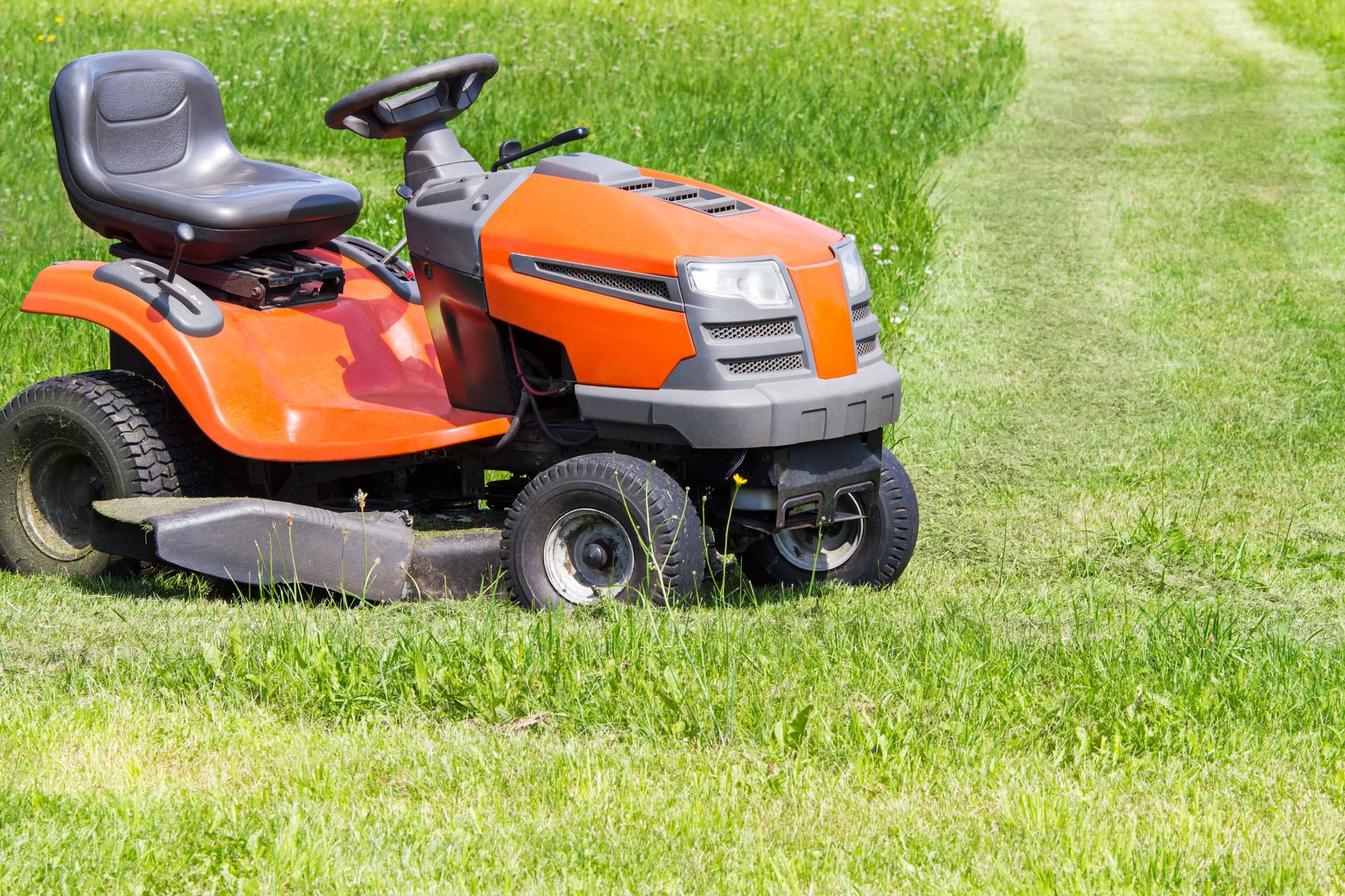 Orange riding lawn mower parked on a grassy lawn during mowing.
